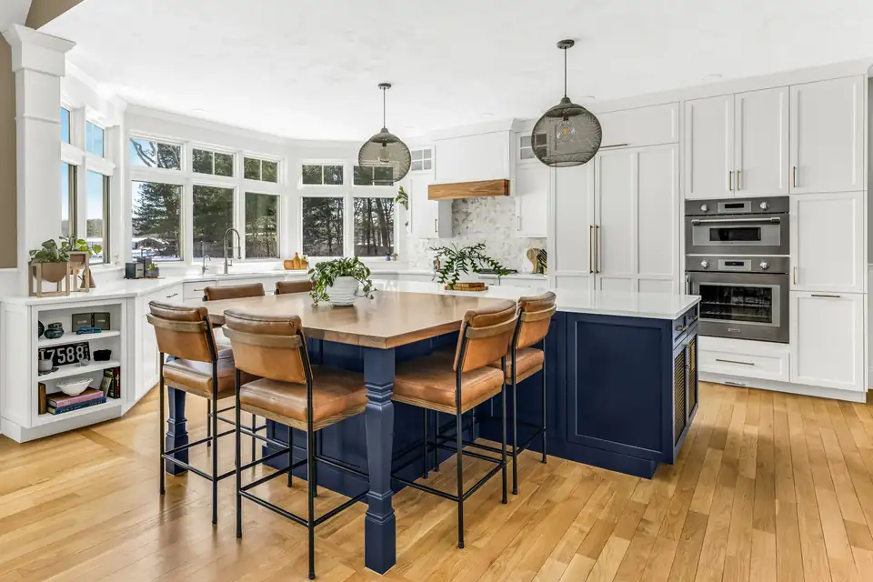 Kitchen remodeling Norwell MA project: white perimeter cabinets, a deep navy island, leather counter stools and glass pendant lights