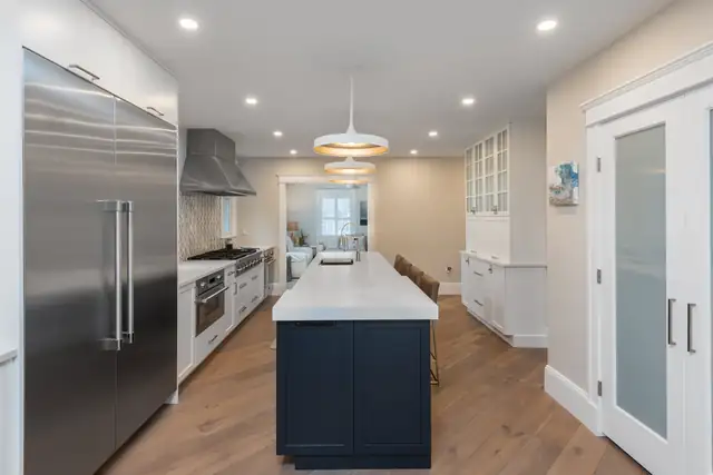 Hingham kitchen with a navy island, white Mouser cabinetry, a built-in stainless refrigerator and wide plank wood floors